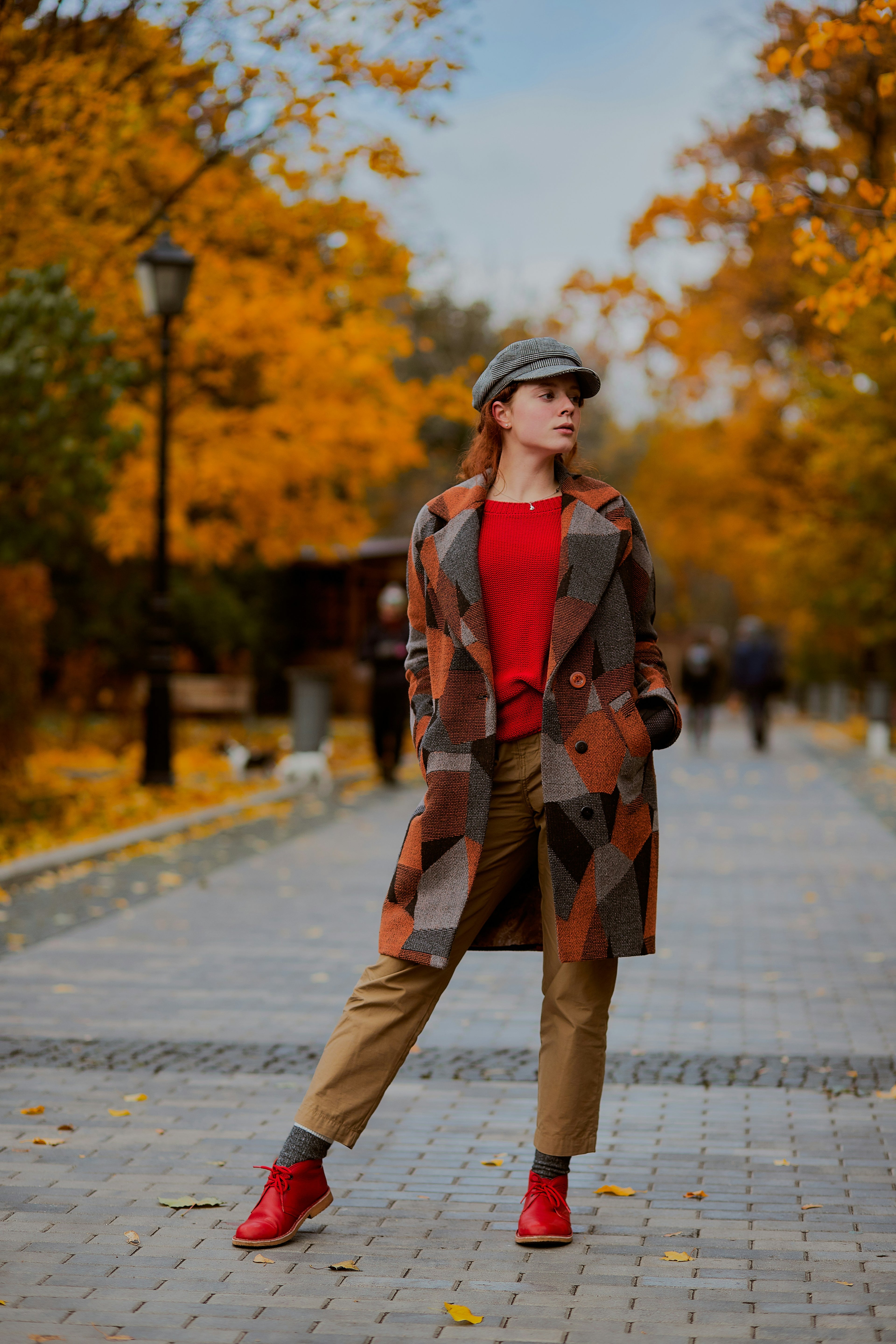 Person wearing a patterned coat and red shoes in an autumn park.